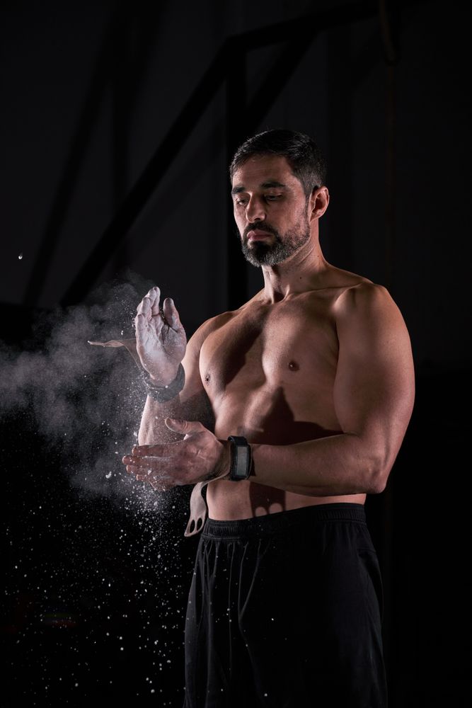 Muscular sportsman clapping hands with magnesium while preparing