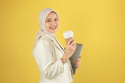 Asian Business Woman in Cream Suit and Hijab Holding a Laptop and Hot Coffee Cup