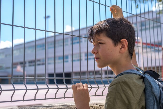 Boy holding fence looking into school yard