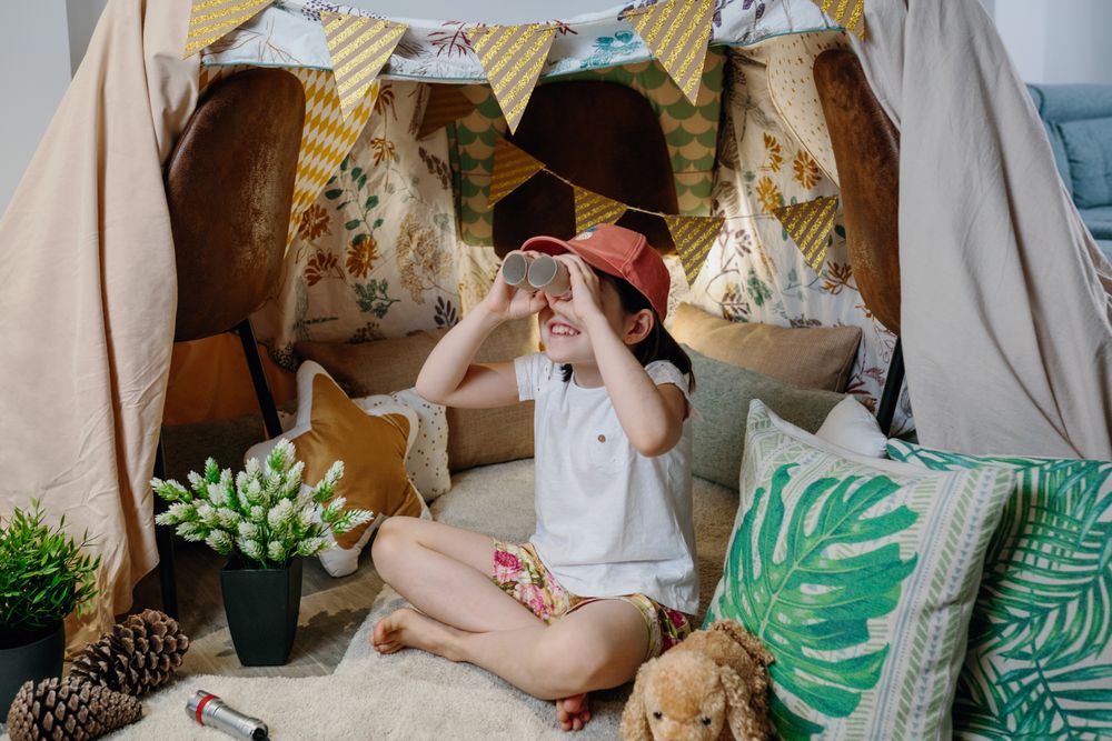 Girl playing with cardboard binoculars while camping at home