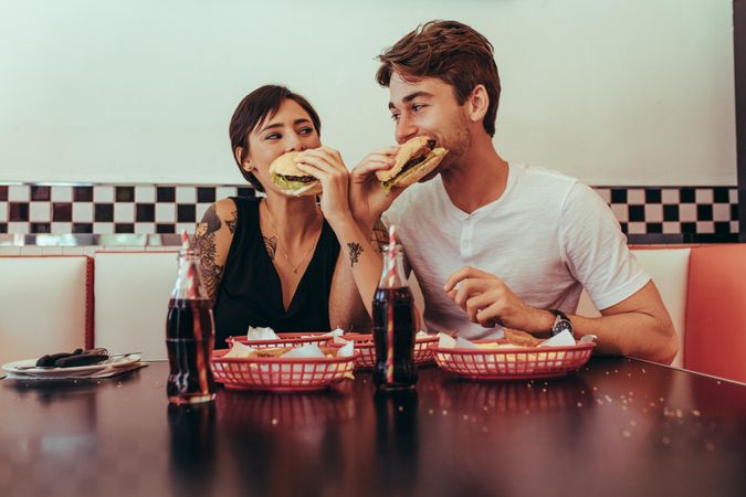 Couple at a restaurant eating burgers with soft drinks on the table