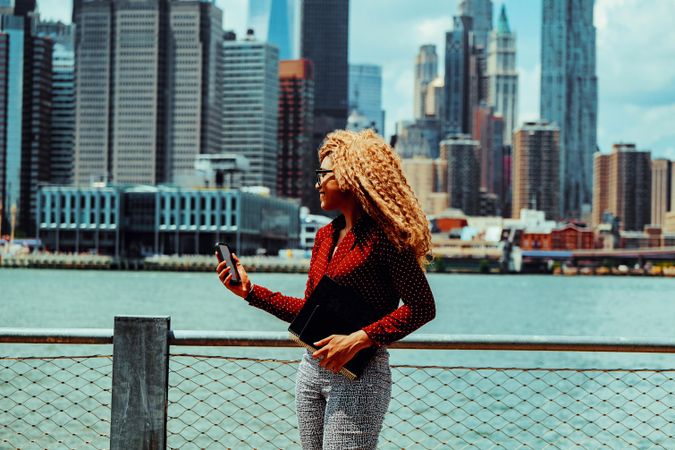 Smiling professional Black female checking phone with Manhattan in the background