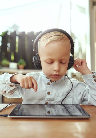 Smiling blond boy using headphones listening to something on digital tablet, vertical