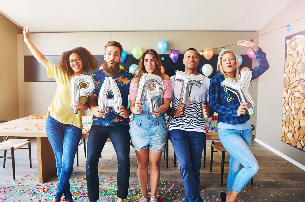 Multi-ethnic friends standing in a line holding silver balloons that say “party”