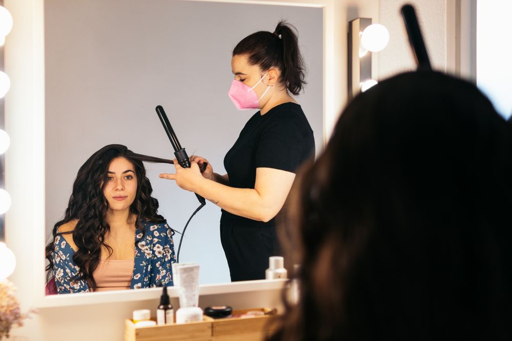 Hairdresser in a mask doing a woman's hair at a dressing table