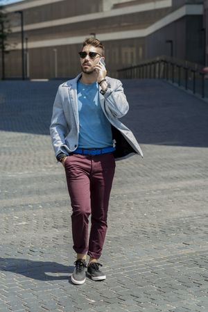 Portrait of cheerful modern businessman speaking on the phone phone and walking outdoors