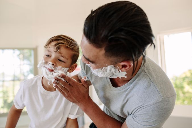 Man applying shaving foam in his sons face in bathroom