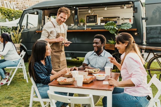 Friendly waiter taking order from diverse friends near food truck