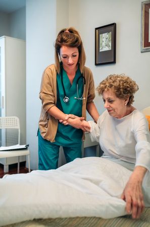Caregiver helping older patient to get out of bed