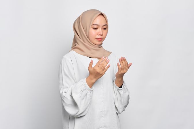 Calm Muslim woman in headscarf and light blouse with hands up in prayer
