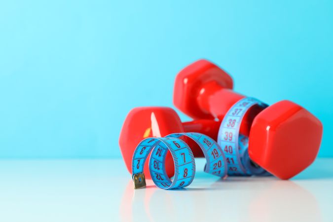 Dumbbells and measuring tape on table against blue background