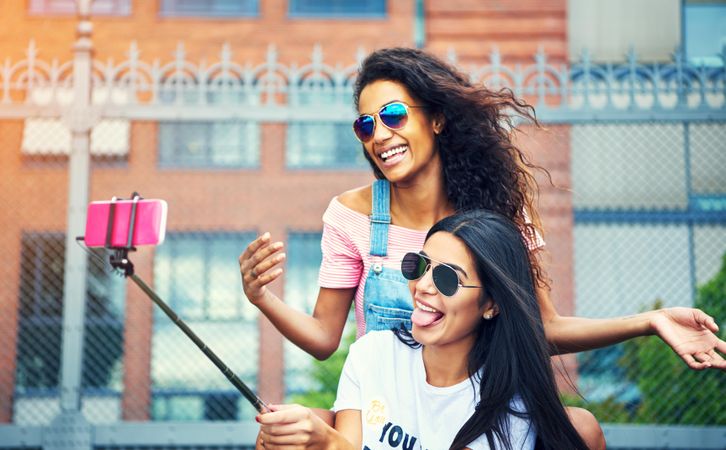 Youthful women using selfie stick to take silly picture on smart phone