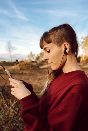 Young woman with piercing listening music on smartphone on hill