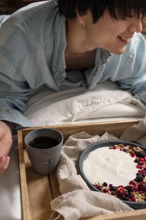 Woman smiling and sitting beside a tray of breakfast and coffee on bed