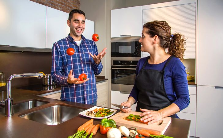 Woman cutting vegetables to prepare food while her husband juggles tomatoes