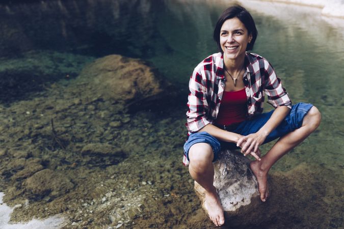 Cheerful woman sitting on rock in clear water