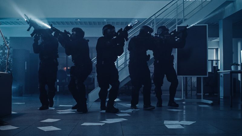 Masked Team of Armed SWAT Police Officers Move in a Hall of a Dark Seized Office Building with Desks and Computers.