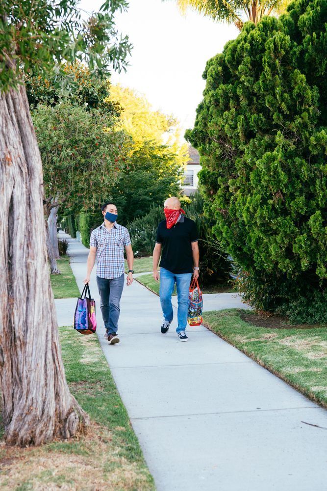 Two men in COVID masks walking back from grocery store with bags of food