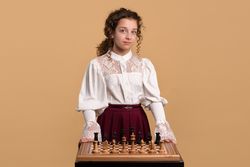 Young girl in white blouse standing behind chessboard