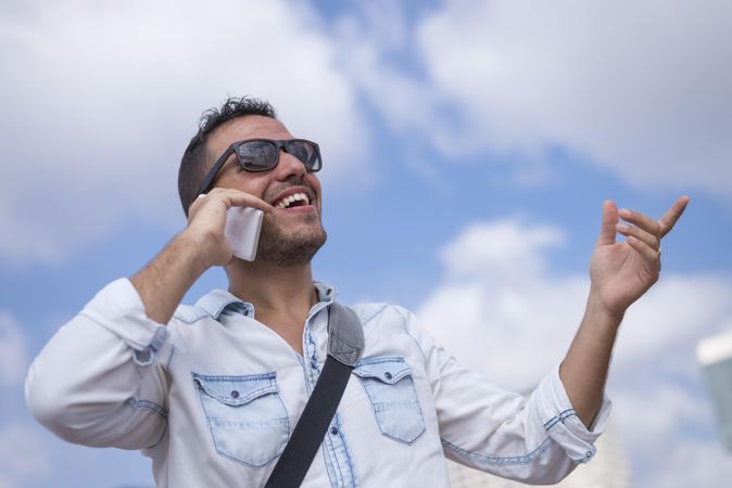 Laughing male having conversation on cell phone with sky in background