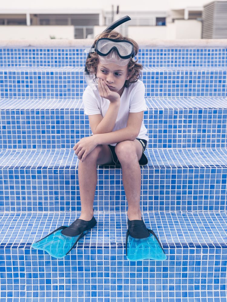 Disappointed preteen boy in diving mask and flippers on poolside