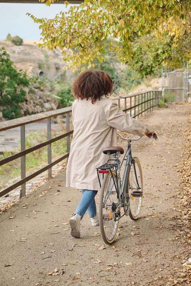 Unrecognizable woman walking with bicycle on road in park