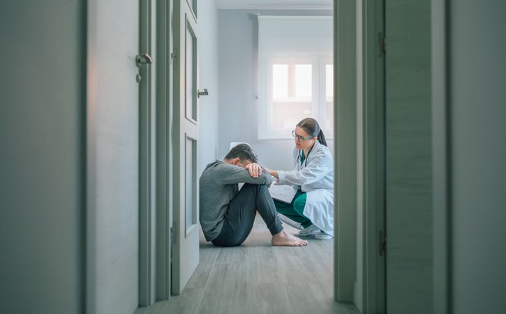 Doctor reassuring and helping to patient sitting on room floor
