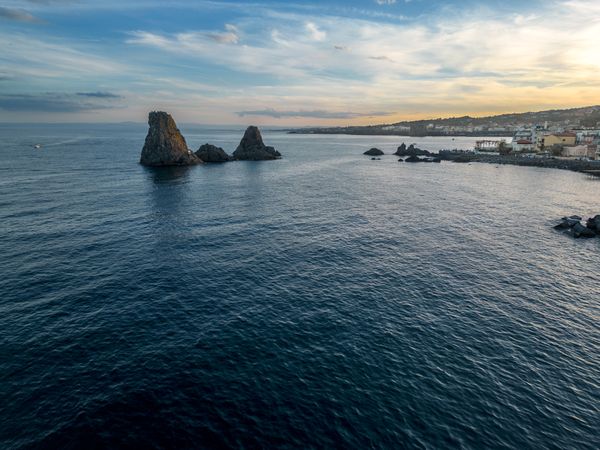 Faraglioni of Acitrezza - majestic sea stacks against the sunset's glow - serene dusk over the Sicilian coastline.