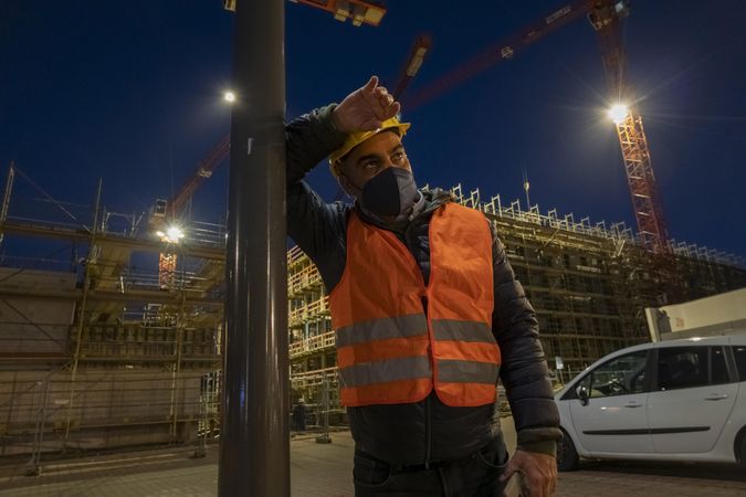 Tired and pensive construction worker with facemask outdoors at night