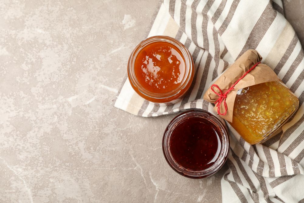 Napkin and glass jars with jam on gray background, top view