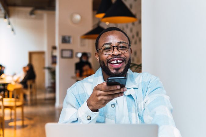Smiling Black man recording voice message in cafe