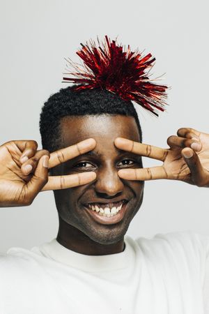 Smiling Black man making the peace sign with a red pompom on his head