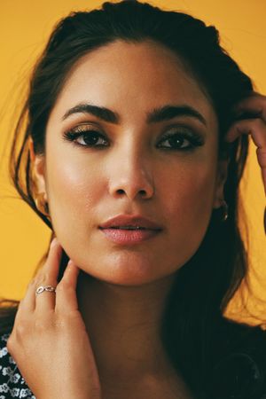 Headshot of Hispanic woman looking at camera in yellow room touching her hair, vertical