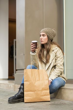 Female sitting outdoors with a take away coffee after shopping