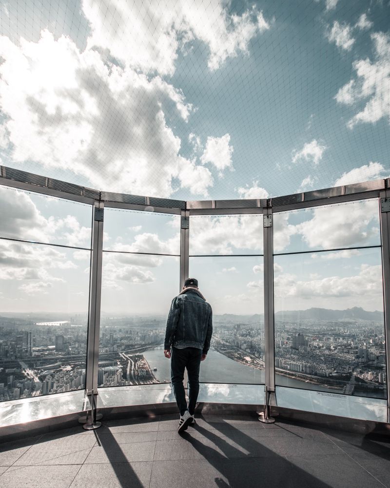 Back view of a man in denim jacket standing on a rooftop of skyscraper looking down the city