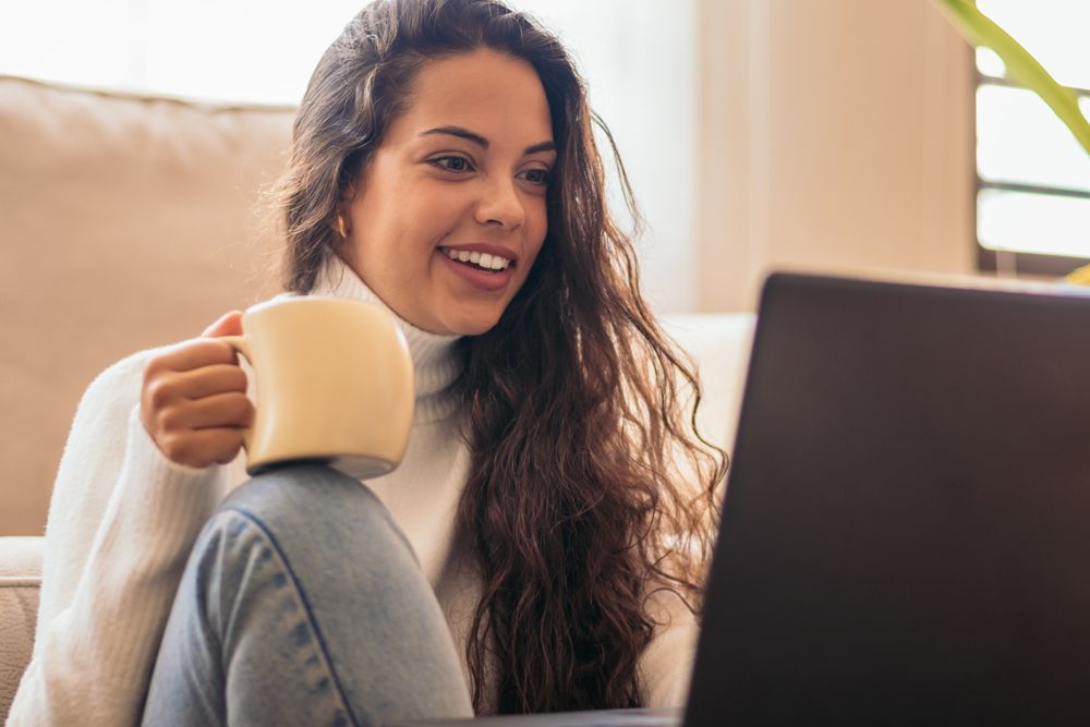Young Woman Enjoying a Cup of Coffee While Using Laptop"