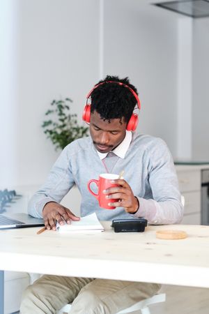 Tired Black economist in headphones with coffee working at home