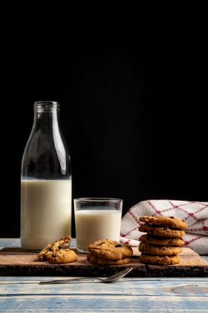 Milk and fresh cookies on board near napkin