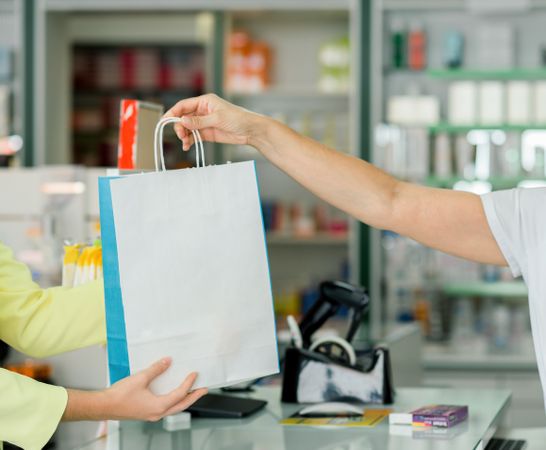 Crop pharmacist giving paper bag with pills to client