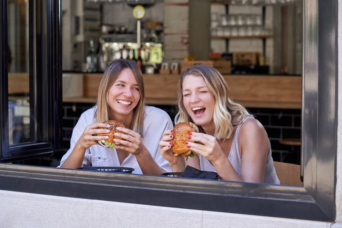 Happy women eating burgers in cafe and having fun