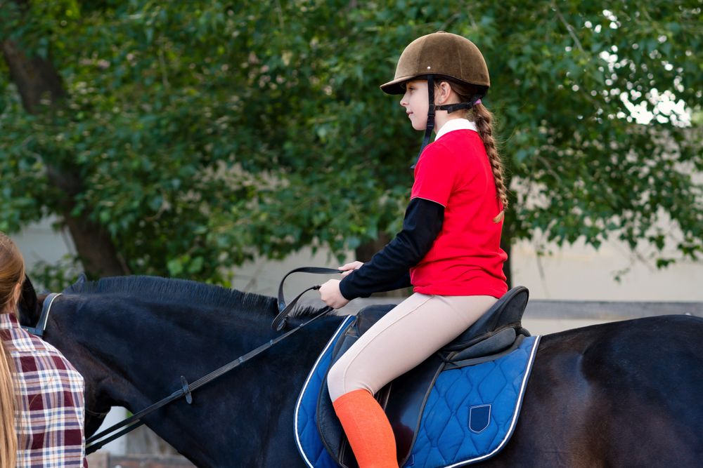Child practices horseback riding under instructor's guidance.
