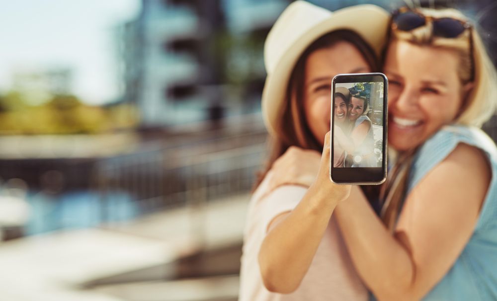 Two women smiling and taking selfie on sunny day
