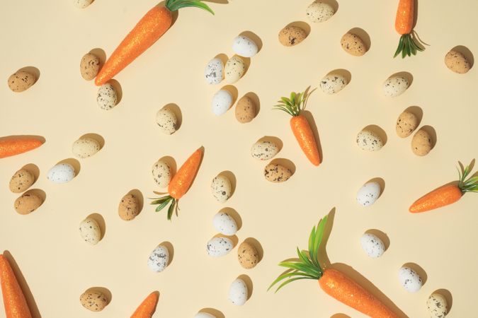 Easter eggs and carrots on pastel yellow background