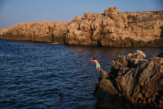 Boy diving into sea from rocks