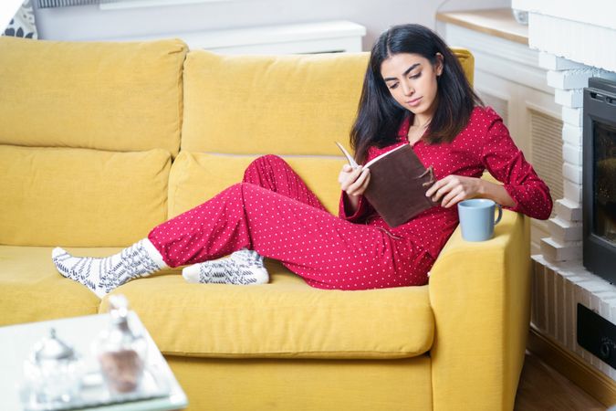 Woman sitting in red pajamas at home reading book
