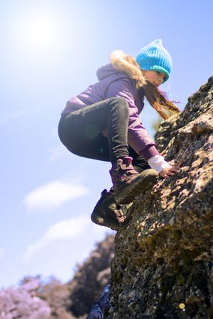 Girl climbing cliff on sunny day