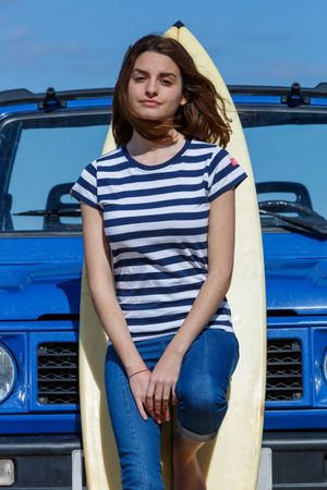 Woman leaning on big surfboard near car