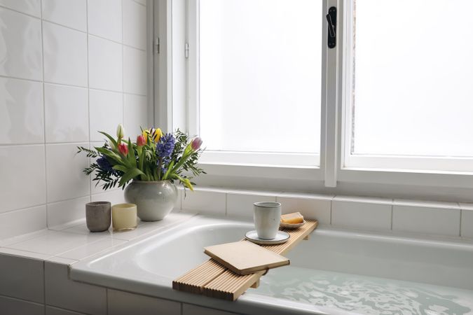 Bathtub with cup of coffee, candles and book, fresh spring bouquet