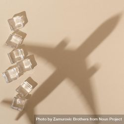 Flat lay of ice cubes on beige background with shadow of airplane 4NYWA5