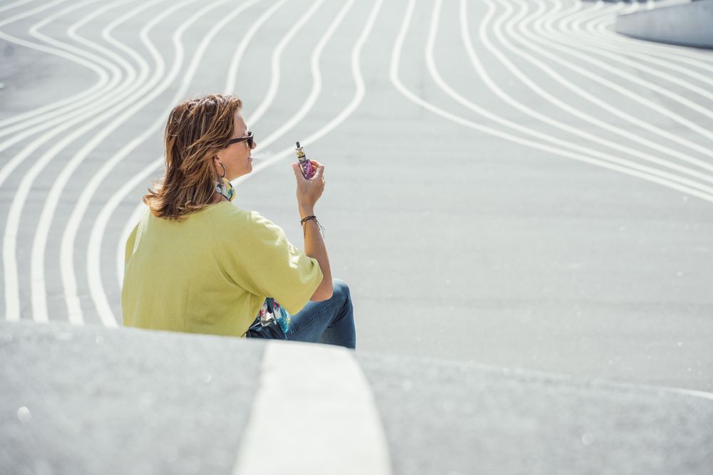 Modern relaxed woman vaping while sitting on marked road